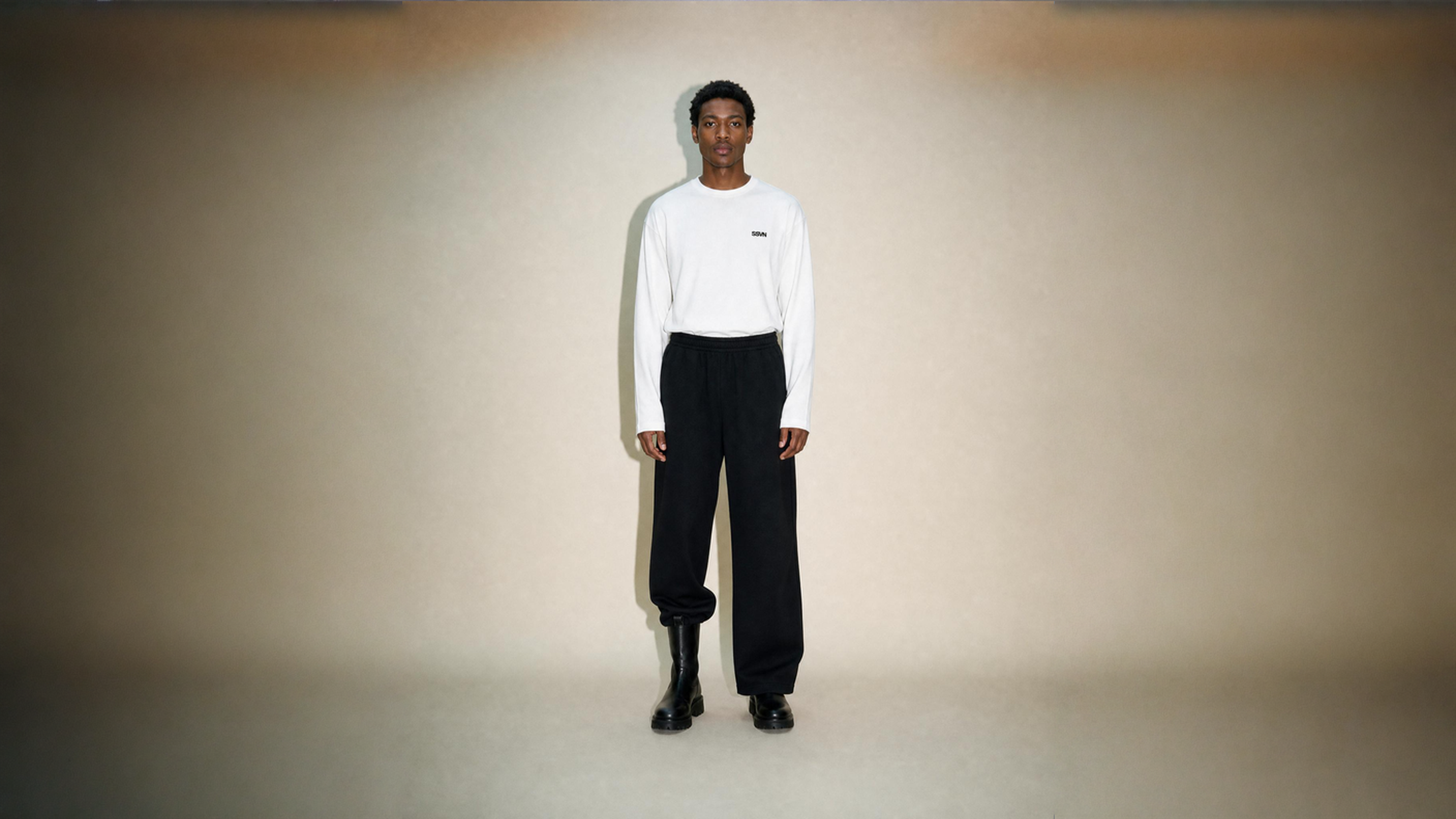 Marcus wearing a white long sleeve core and black sweat pants standing against a plain background